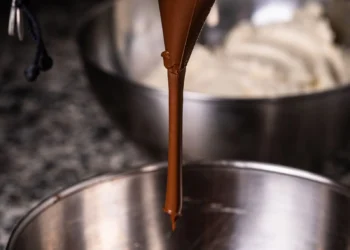 Chocolate derretido sendo despejado em tigela, superfície brilhante (imagem ilustrativa)