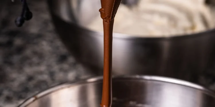 Chocolate derretido sendo despejado em tigela, superfície brilhante (imagem ilustrativa)