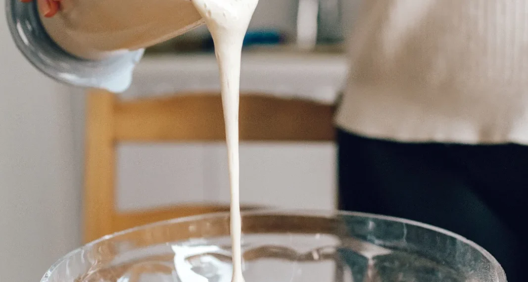 Creme líquido sendo despejado de um recipiente durante o preparo de uma receita