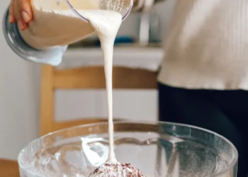 Creme líquido sendo despejado de um recipiente durante o preparo de uma receita