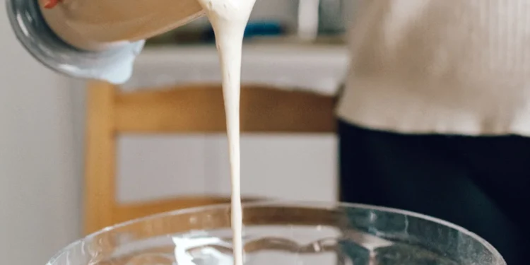 Creme líquido sendo despejado de um recipiente durante o preparo de uma receita