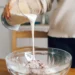 Creme líquido sendo despejado de um recipiente durante o preparo de uma receita