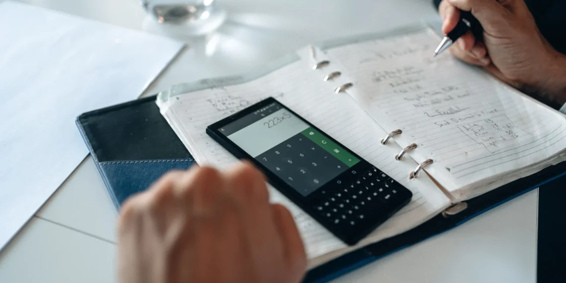 Pessoa anotando cálculos em um caderno ao lado de uma calculadora, planejando custos