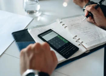 Pessoa anotando cálculos em um caderno ao lado de uma calculadora, planejando custos