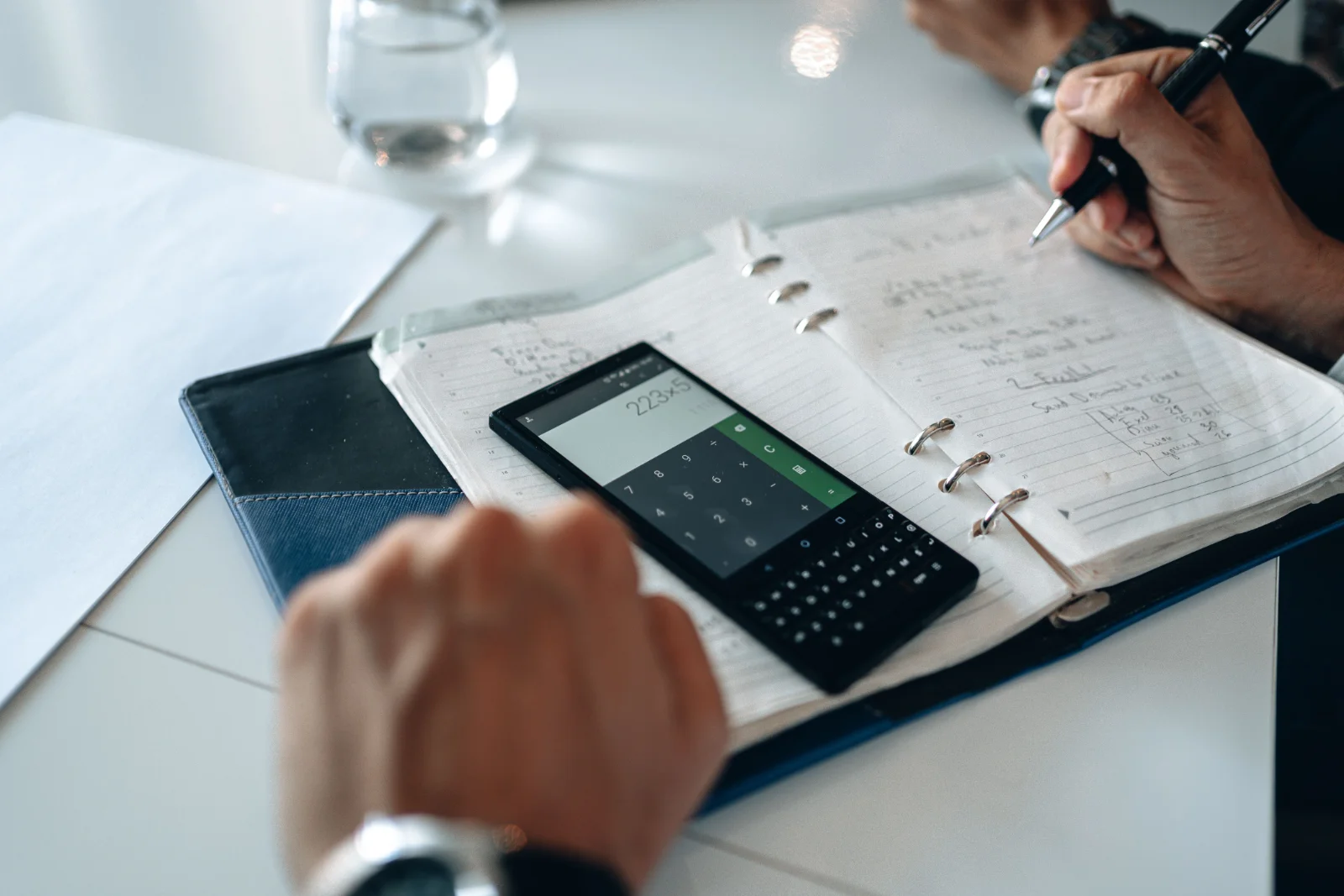 Pessoa anotando cálculos em um caderno ao lado de uma calculadora, planejando custos
