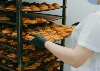 Pessoa retirando uma bandeja de doces assados de uma prateleira organizada de produção