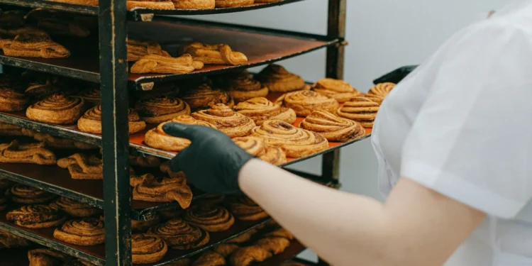 Pessoa retirando uma bandeja de doces assados de uma prateleira organizada de produção