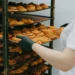 Pessoa retirando uma bandeja de doces assados de uma prateleira organizada de produção