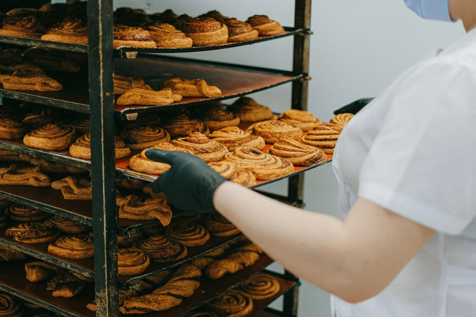 Pessoa retirando uma bandeja de doces assados de uma prateleira organizada de produção